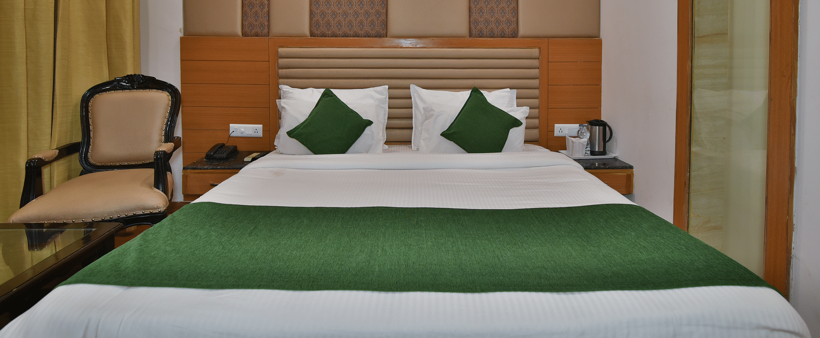 A large bed placed next to chair in Deluxe Room at DLS Highland Resort and Spa, Mussoorie.